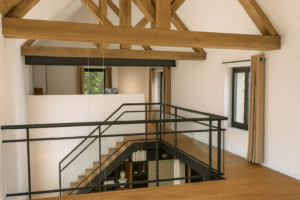 Aménagement d'un étage avec mezzanine à Tarbes : charpente en bois massif apparente, garde-corps industriel en métal noir et vue plongeante sur l'escalier design.